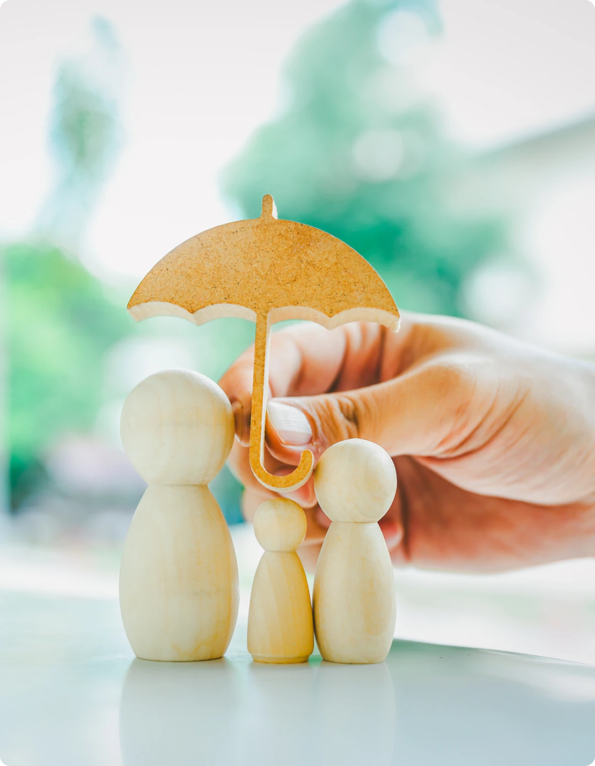 Hand holding umbrella over wooden figures.